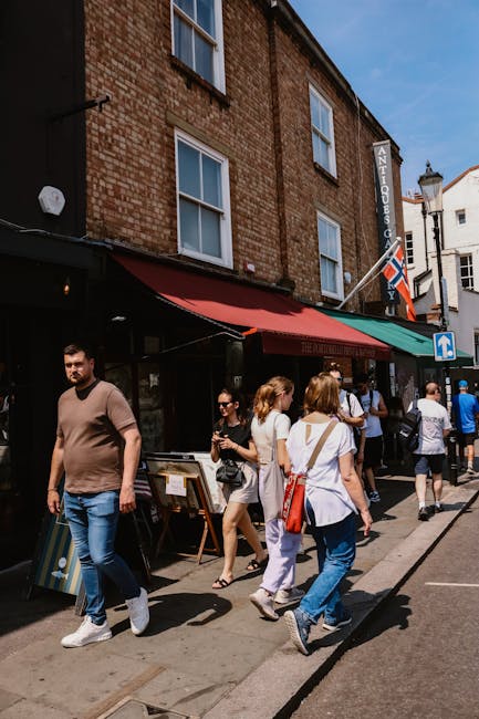 A street scene in Notting Hill showing a large banner hanging above the road, decorated with British Union Jack flags on either side. The banner reads 'Portobello Road Market Tips,' and the surroundin